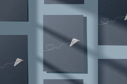 Dunkelblaue Klappkarte mit Papierflieger-Motiv und gepunkteter Linie in Herzform, mehrfach arrangiert in einem grafischen Mockup auf hellblauem Hintergrund. Die Grußkarte aus Recyclingpapier eignet sich als Hochzeitskarte, Valentinstag Karte, Karte zum Jahrestag oder Freundschaftskarte. Design von My Pretty Circus.